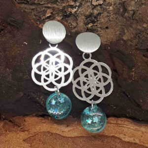 Silberne Ohrringe mit Ohrringstecker mit gebürsteter Oberfläche, silbernem Metallornament in Form einer Lebensblume und einem ovalen türkis gefärbten Epoxidharz Anhänger mit kleinen Glitzersternchen