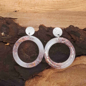 Creolen aus Epoxidharz, gefärbt in weiß und rosa mit Glitzer; am Ohr gehalten durch einen runden, silbernen Ohrringstecker mit glitzernder Oberfläche